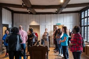 A group of people standing inside the Great Hall at Blakesley Hall, listening to a member of staff