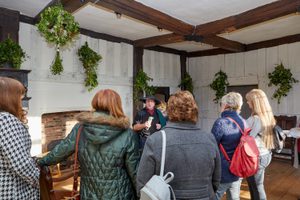 Back of group of visitors listen to a guided tour in a historic Tudor room.