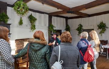 Back of group of visitors listen to a guided tour in a historic Tudor room.