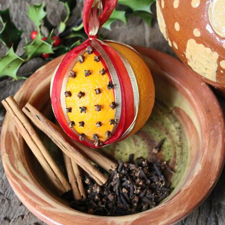 Orange pomander in a bowl with cinnamon sticks and holy, viewed from above.