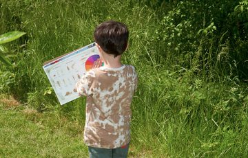 A child is outside in a garden looking a clipboard.