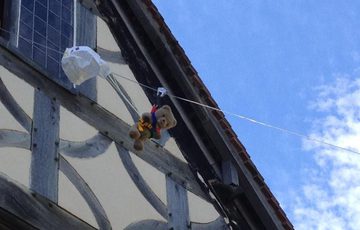 A teddy with a harness and paper parachute coming out of a window and going down a zip wire.