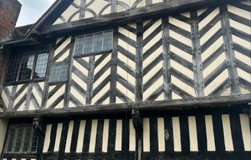 A teddy bear in a basket half way down the zip wire that is attached from the top window of an historic Tudor building.