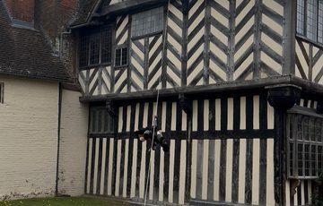 Historic Tudor building with a wire coming out of the top floor window to the floor, a teddy is half way down the wire.