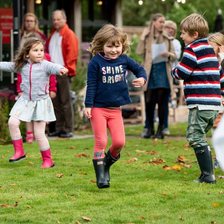 A group of children are outside in a garden dancing.