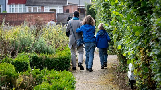 A family inlcuding a adult and two children, walking down a path surrounded by shrubs. They face away from the camera.