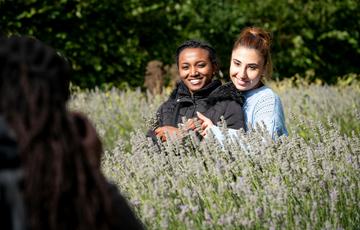 A lady hugging another lady from behind. They are smiling and posing for someone who is taking a photo..