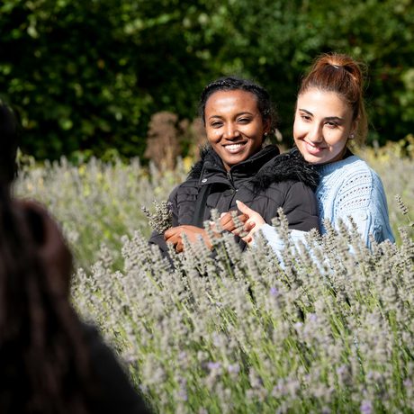 A lady hugging another lady from behind. They are smiling and posing for someone who is taking a photo..