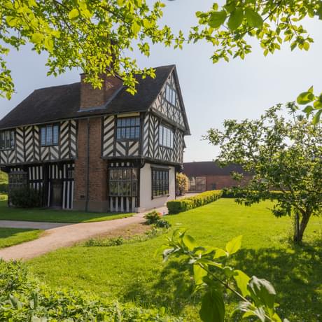 Tudor timber-framed house in garden surrounded by trees