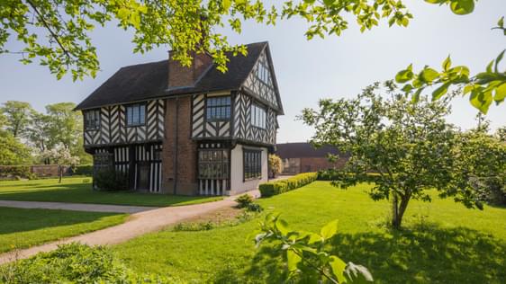 Tudor timber-framed house in garden surrounded by trees