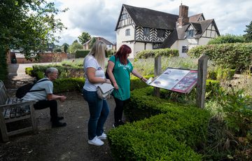 Two ladies reading an information in the garden. Another person sits on a nearby bench. Blakesley Hall Tudor building is in the background.