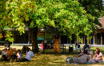 Groups of adults and children having picnics in a garden under a tree.