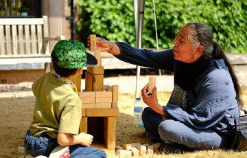 An adult and child play a game of garden Jenga outside on the grass.