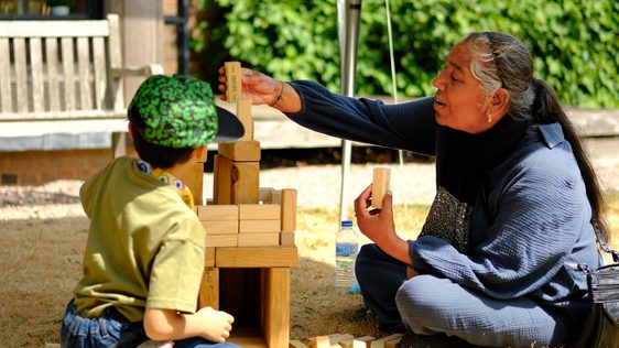 An adult and child play a game of garden Jenga outside on the grass.