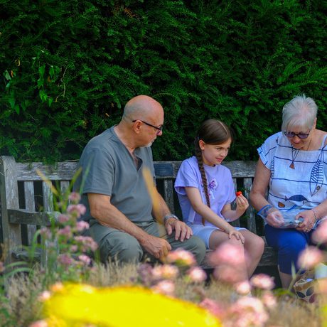 Two adults and a child sitting on a garden bench.