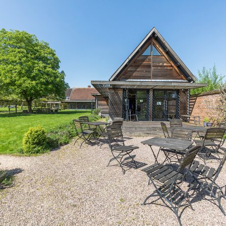 Outdoor seating with metal tables and chairs near a wooden A-frame building and green lawn.