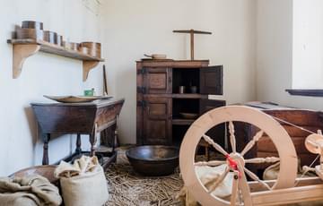 A small room with spinning wheel, desk and cupboard.
