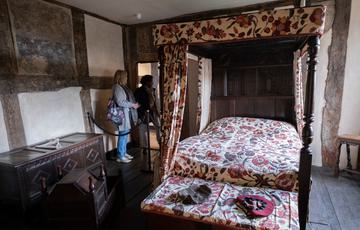 Two visitors looking into an historic room with four poster bed.