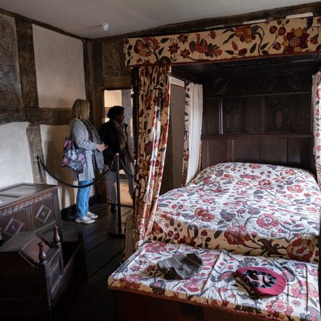 Two visitors looking into an historic room with four poster bed.