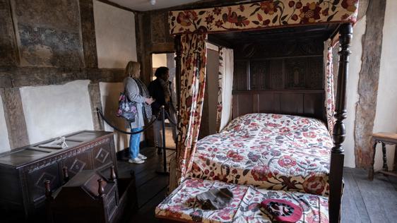 Two visitors looking into an historic room with four poster bed.