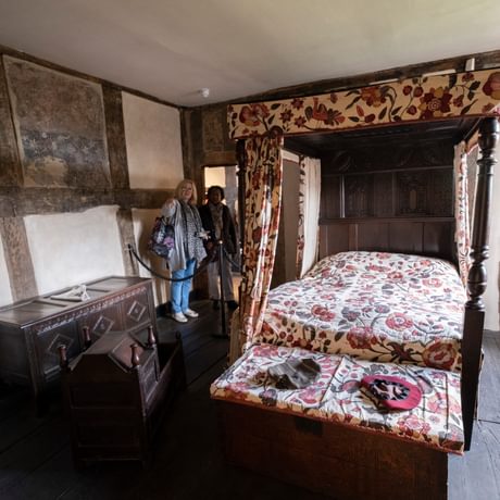 Two visitors looking into an historic room with four poster bed.