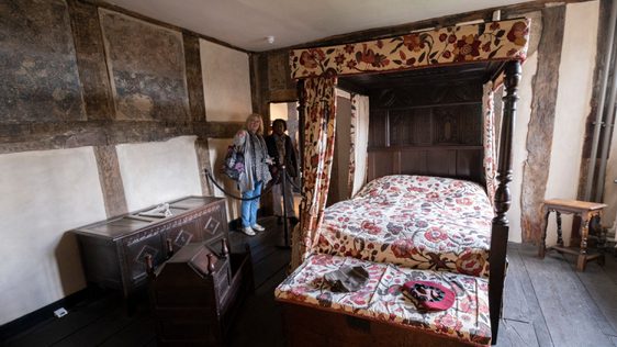 Two visitors looking into an historic room with four poster bed.