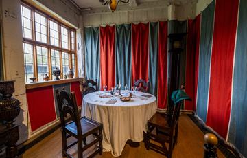 A small room with red and blue fabric hung around the room and small circular table with chairs in the centre.