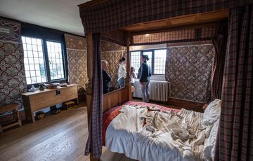 Visitors looking out of window of an historic bedroom with a four poster bed.
