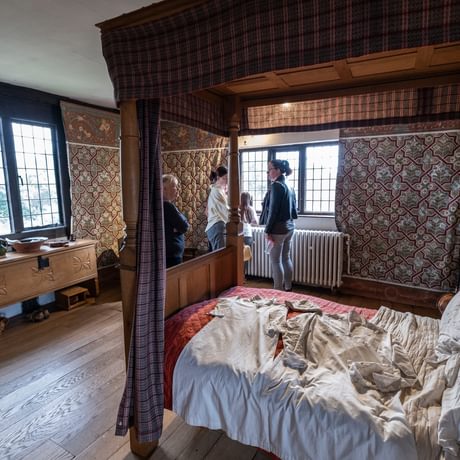 Visitors looking out of window of an historic bedroom with a four poster bed.