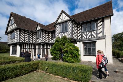 Exterior view of a Tudor timber-framed house with adults and children walking in the garden.