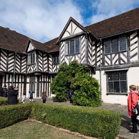 Exterior view of a Tudor timber-framed house with adults and children walking in the garden.
