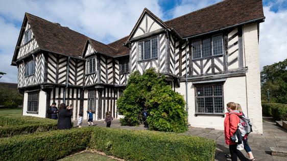 Exterior view of a Tudor timber-framed house with adults and children walking in the garden.