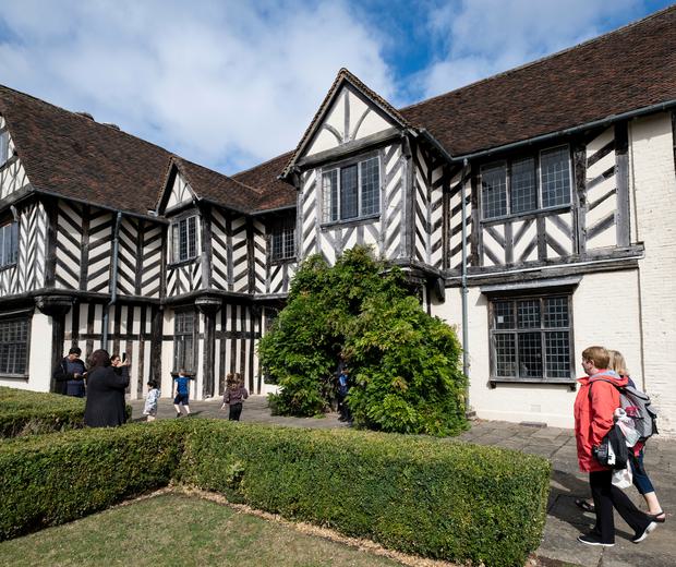 Exterior view of a Tudor timber-framed house with adults and children walking in the garden.