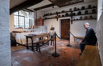 A visitor sat on a bench looking at an Tudor style kitchen.