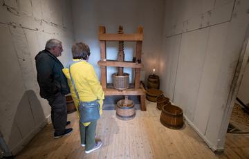 Two visitors in a small room with an old wooden machine and barrells.