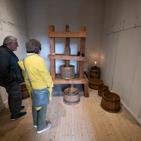 Two visitors in a small room with an old wooden machine and barrells.