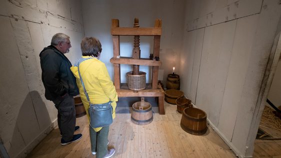 Two visitors in a small room with an old wooden machine and barrells.