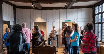 A group of people standing inside the Great Hall at Blakesley Hall, listening to a member of staff