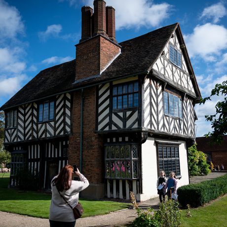 Exterior view of a Tudor timber-framed house with an adult taking a photo of two children in front of the building.