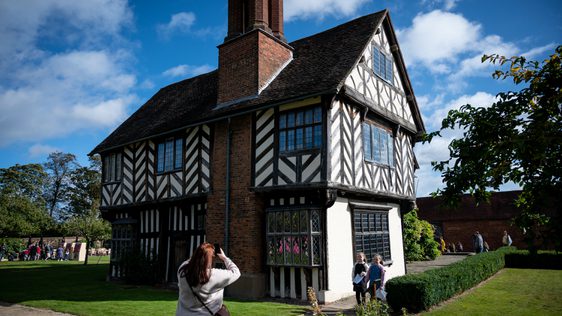 Exterior view of a Tudor timber-framed house with an adult taking a photo of two children in front of the building.