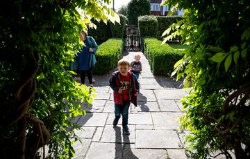 Green foliage frames two children walking through it.
