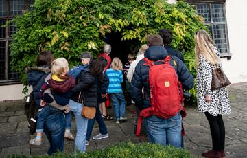 An exterior of a Tudor house, with a group of adults and children entering through the front door.