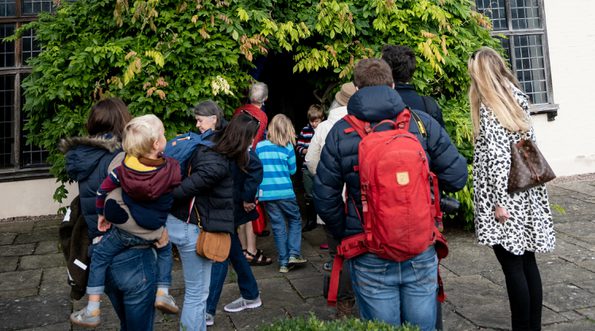 An exterior of a Tudor house, with a group of adults and children entering through the front door.