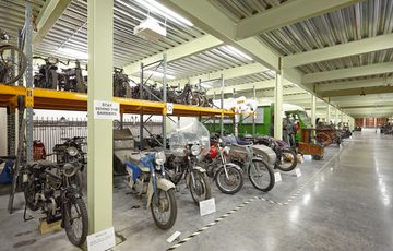 Large storage room containing vintage motorcycles and cars