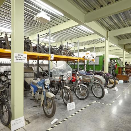 Large storage room containing vintage motorcycles and cars