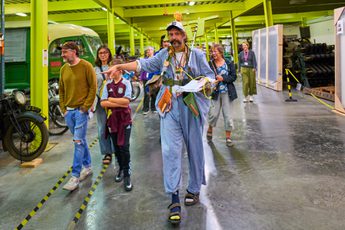 Man in quirky blue outfit leads group through museum store.