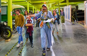 Man in quirky blue outfit leads group through museum store.