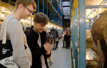 Two people in the collections storage warehouse are smiling while looking at a object on open display.
