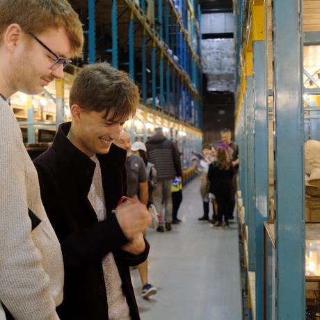 Two people in the collections storage warehouse are smiling while looking at a object on open display.