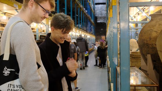 Two people in the collections storage warehouse are smiling while looking at a object on open display.